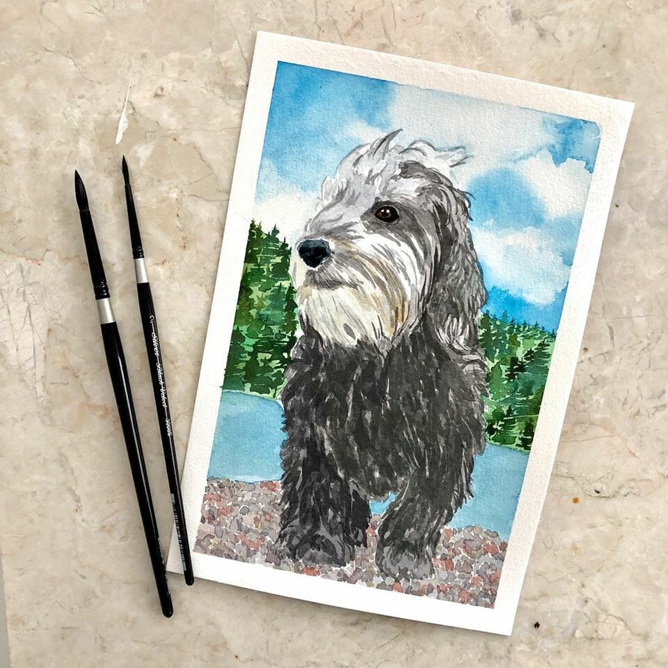 a watercolour painting of a fluffy poddle mix dog on the beach with two paint brushes
