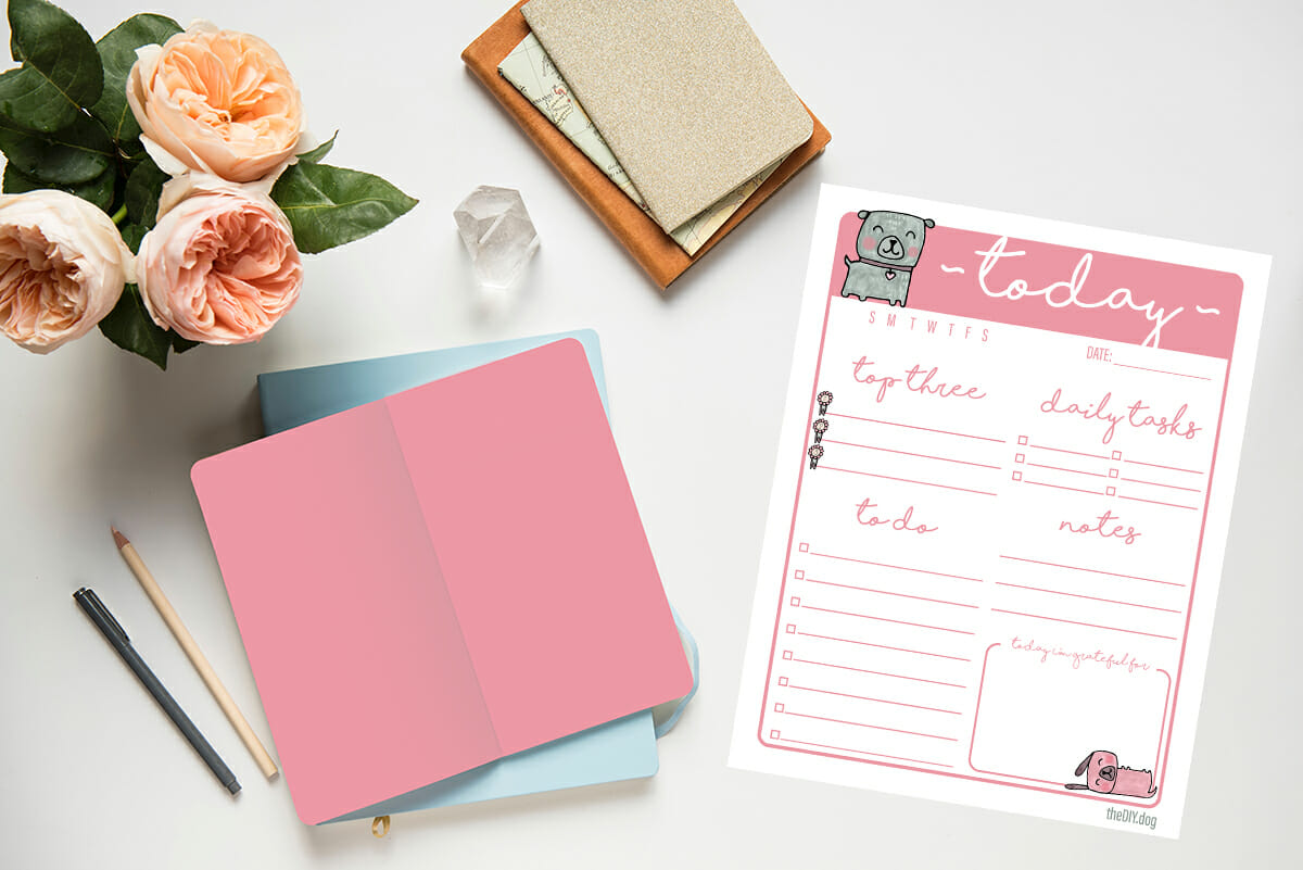 a stack of blank books lay on a white table with a case of pale ink flowers and a free printable daily planner page featuring dog art