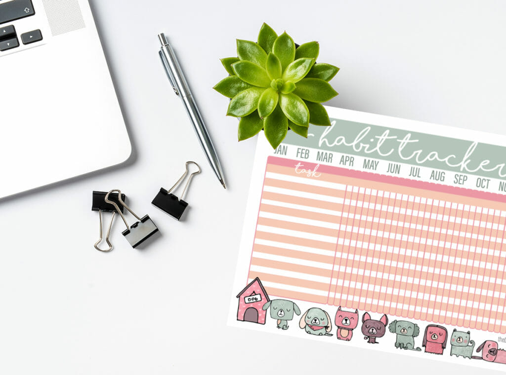 a free printable habit tracker featuring dog art sits on a desk with a succulent plant, a silver pen, several alligator clips and a macbook.