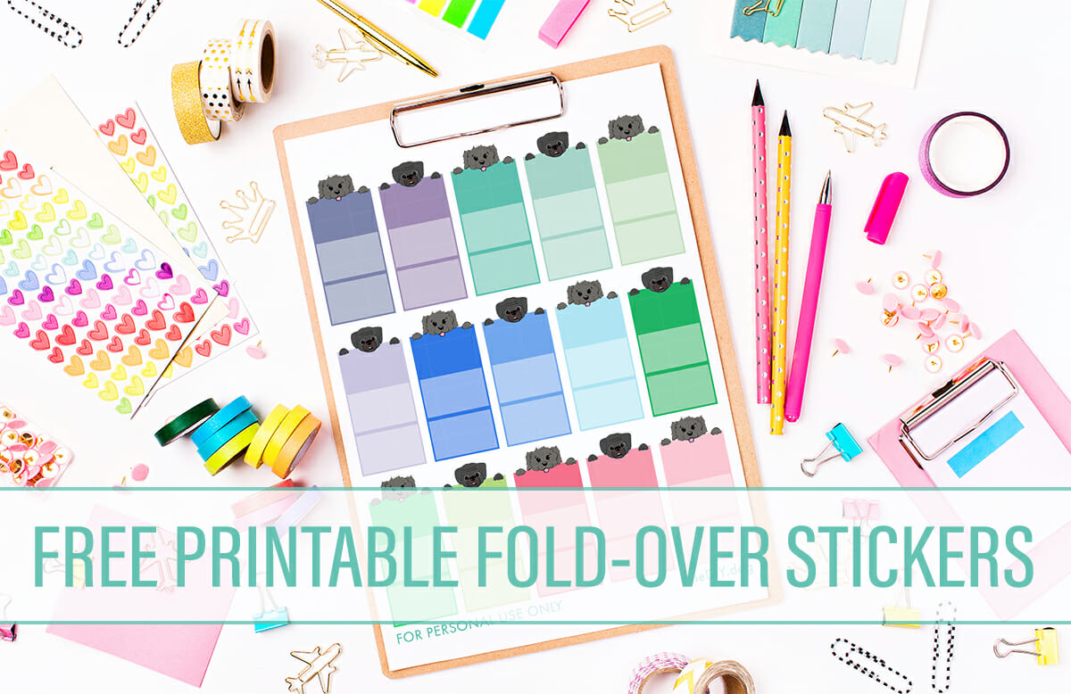 a page of free brightly coloured printable foldable stickers with a black fluffy cartoon dog or a black cartoon puggle dog face peeking over the top of each one lays on a messy table of brightly coloured pens, post its and art supplies