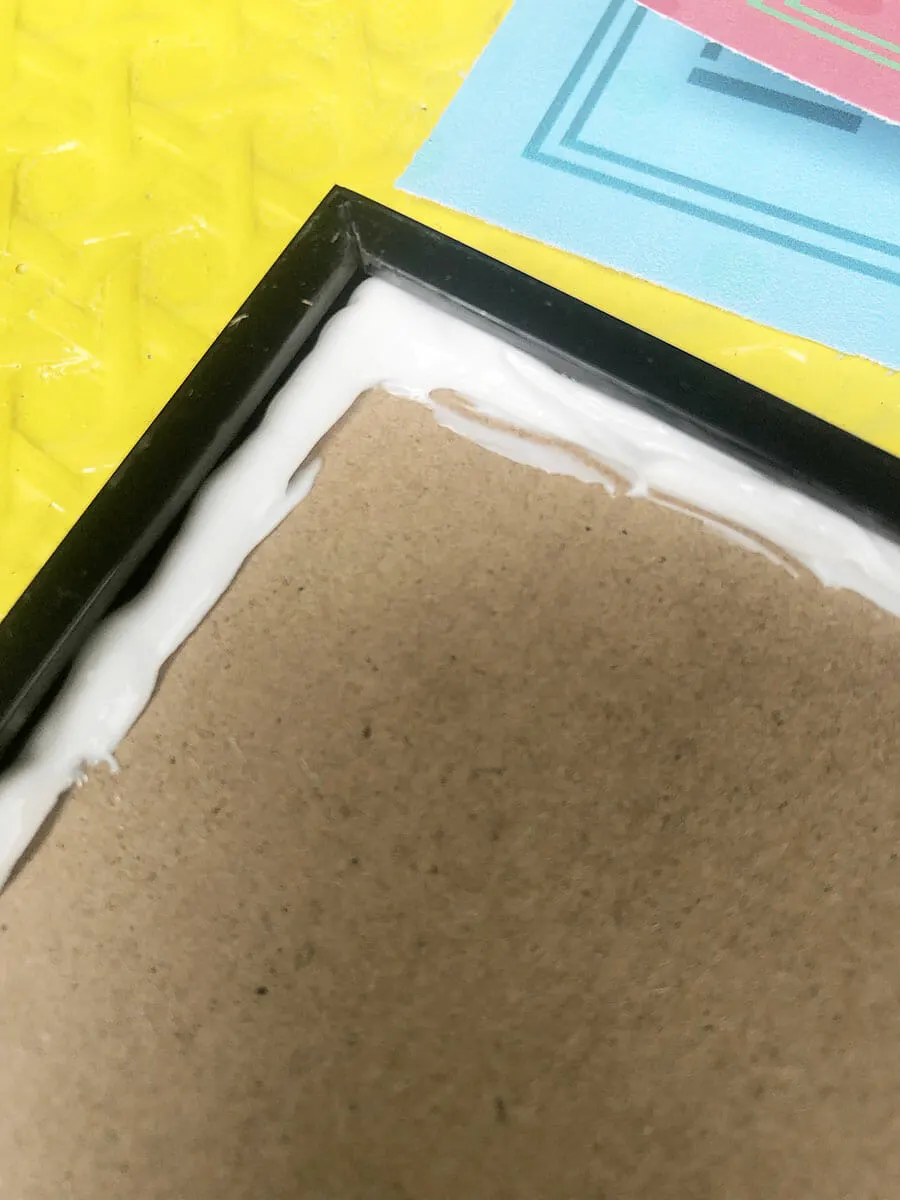 a black picture frame sits on a bright yellow table. There is a bead of construction caulking around the edge of the frame to seal it