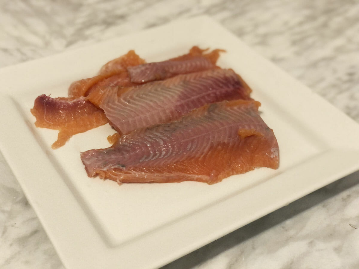 a plate of poorly cut raw trout fillets sits on a square white platter on a marble table