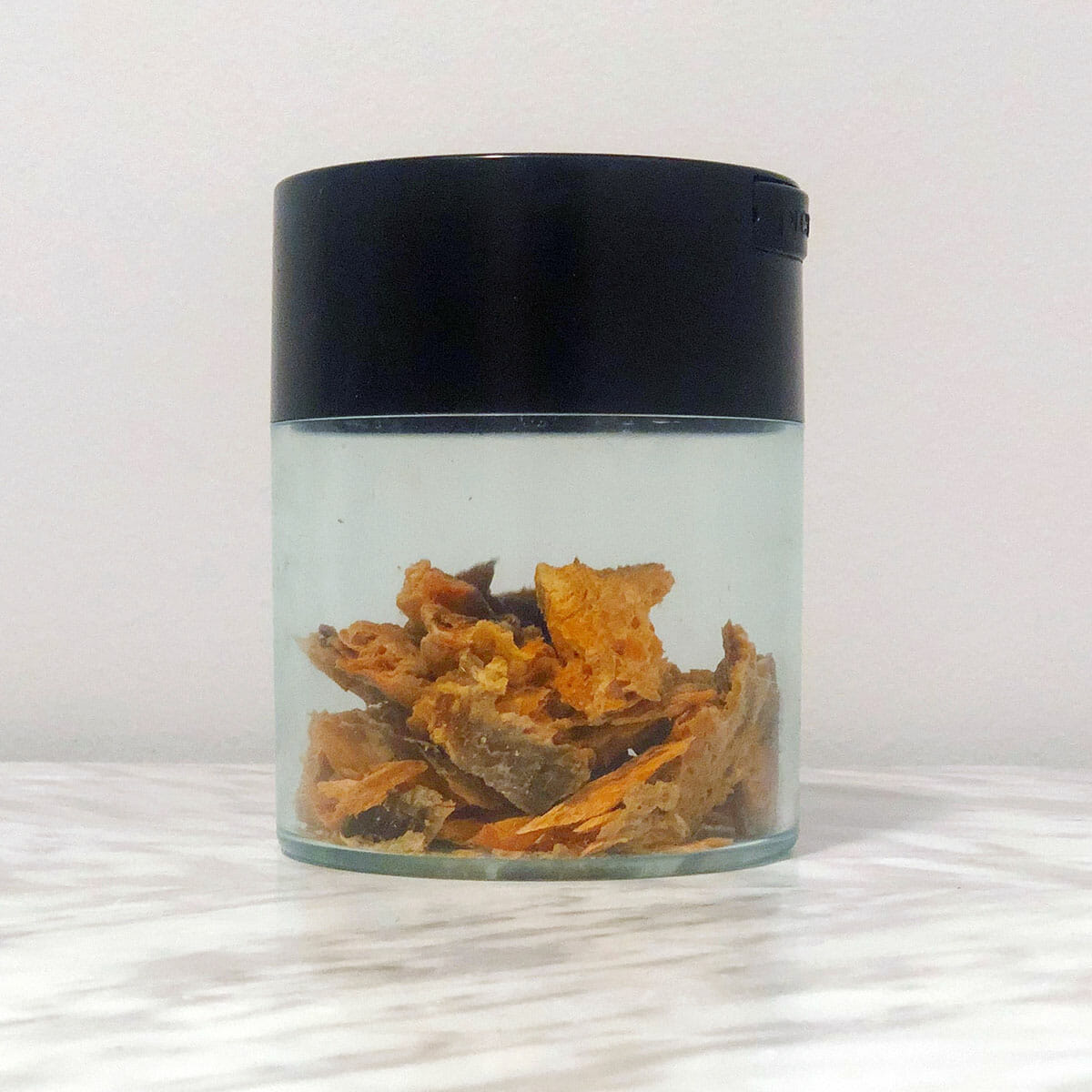 a vacuum sealed storage jar with a black lid half filled with trout jerky pieces sits on a marble table