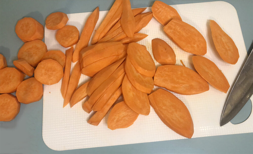 bright orange sweet potatoes sliced on a white cutting board. 